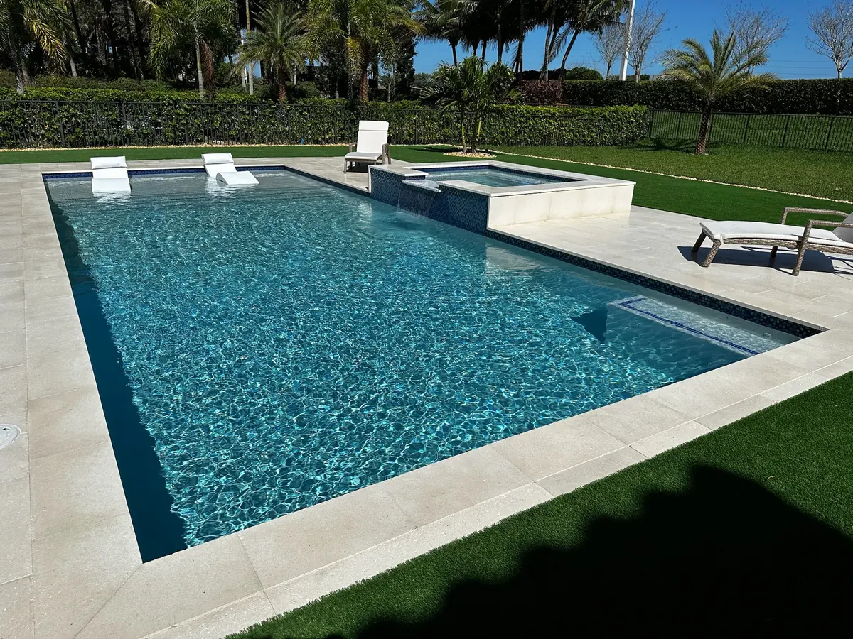 Bright turquoise pool with white in-pool loungers, a raised spa and white coping on a turf lawn