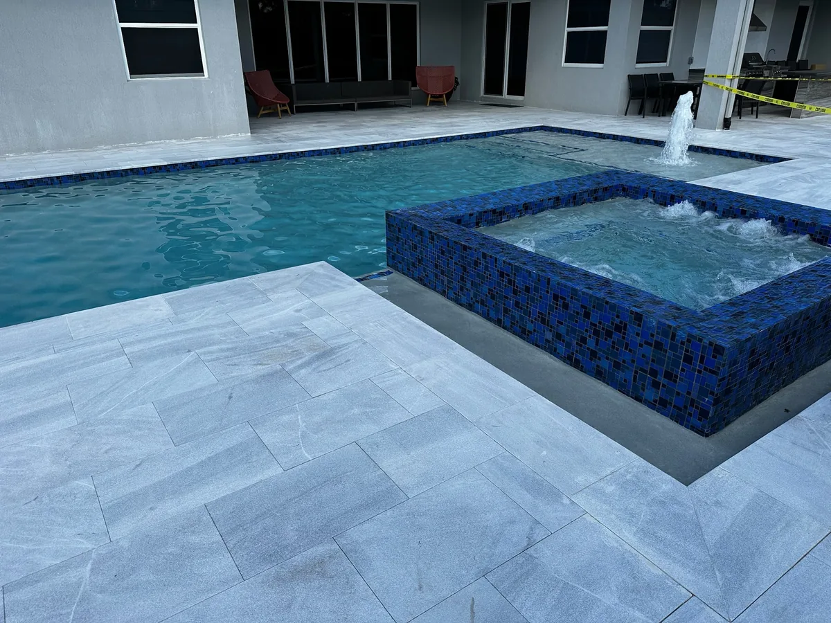 Blue mosaic raised spa with spillover into the pool beside a covered patio and a jet