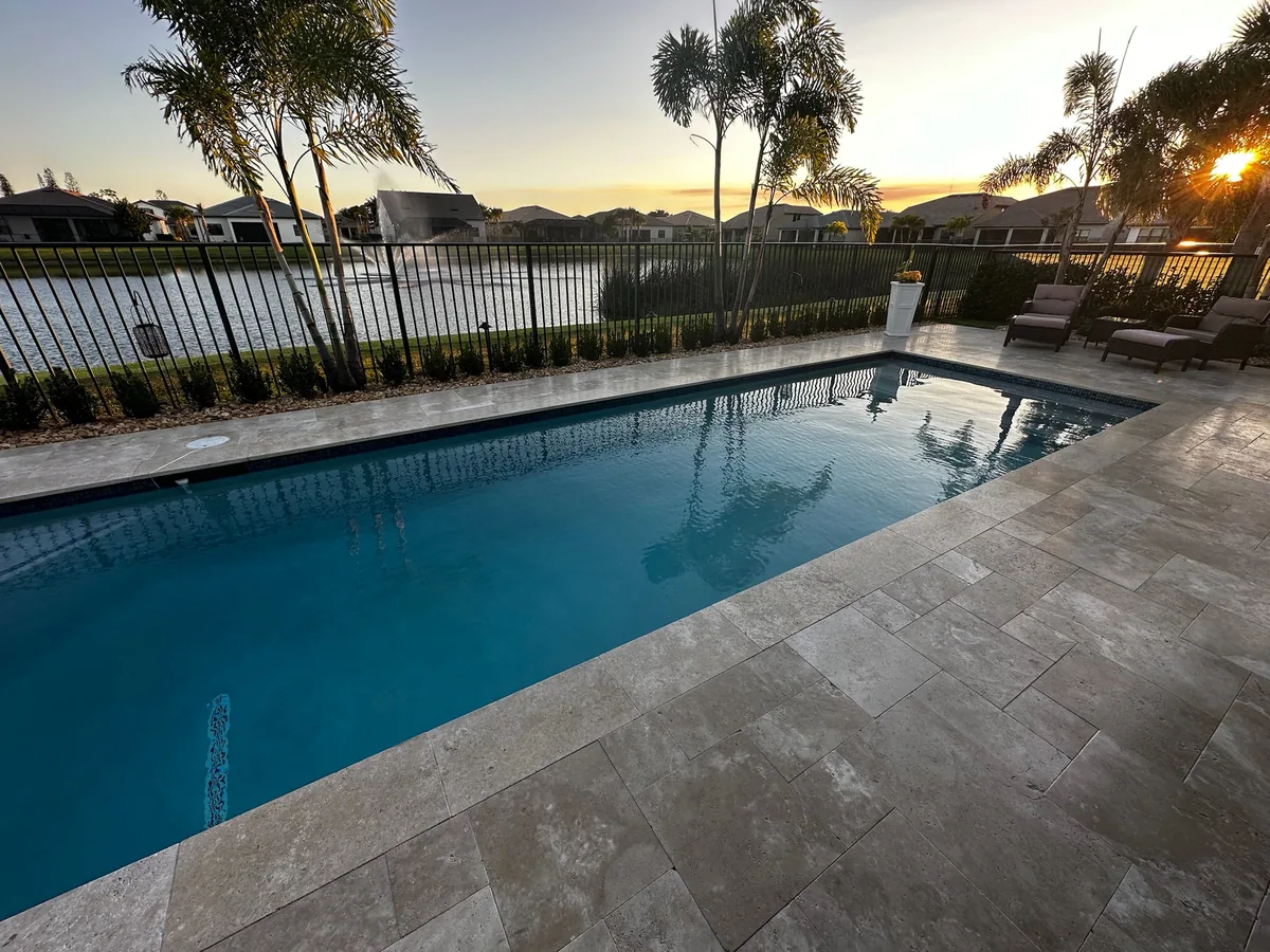 Pool with stone-style deck, black fence and lake view at sunset
